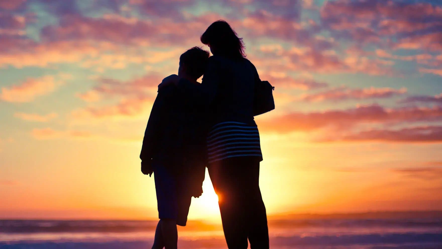 Two people hugging at the beach with sunset in the background